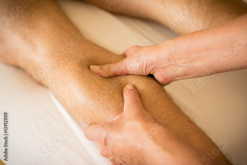 Therapist applying pressure on male leg - hand massage of human calf muscle