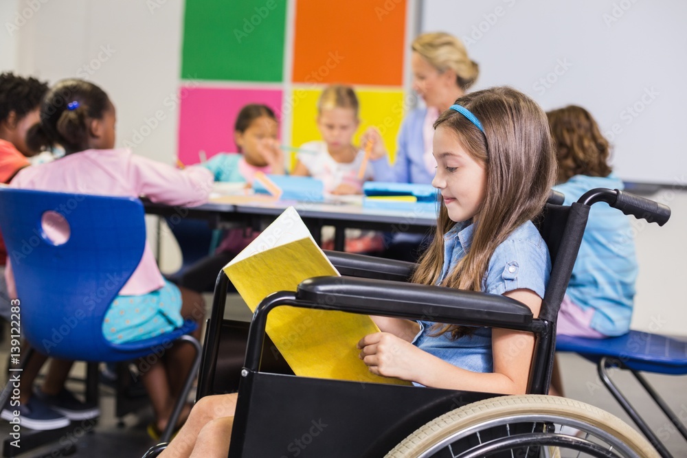 Disabled school girl on wheelchair reading a book in classroom Stock ...