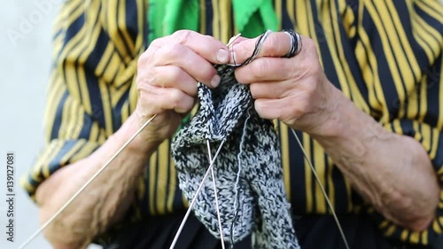Senior woman knits wool socks, close up. Ukrainian old woman is engaged in knitting. Old woman in green headscarf knits sock. Female in kerchief knits wool sock