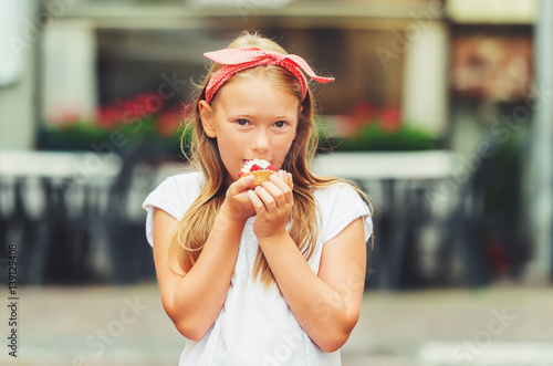 Funny little girl eating cake outdoors, wearing red polka dot head band