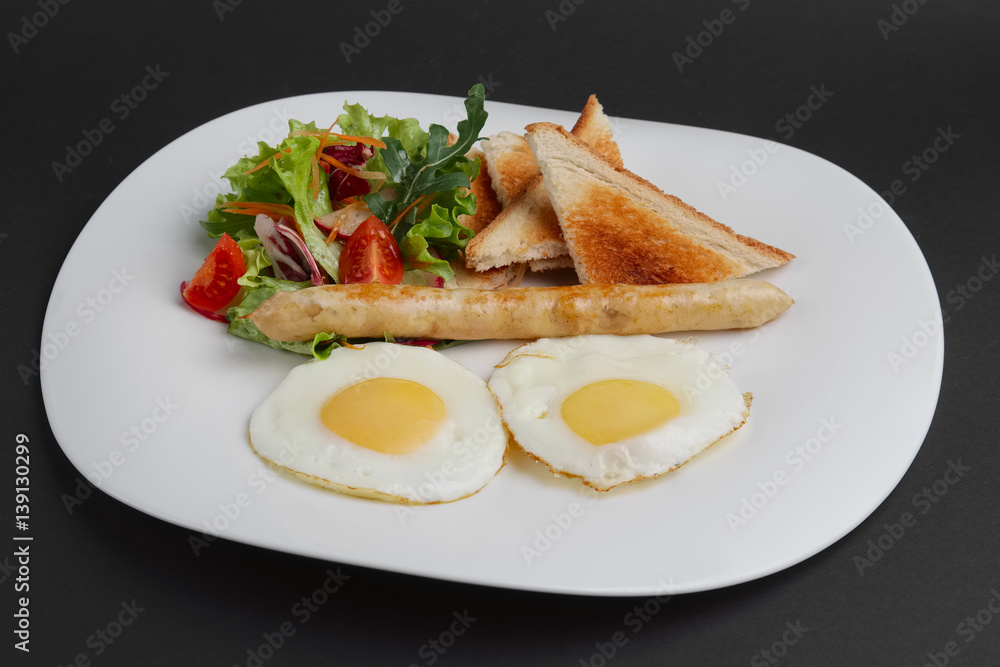 Fried eggs with homemade sausage, toasts and fresh tomato and salad. Fried eggs with homemade sausage, toasts and fresh tomato and salad.