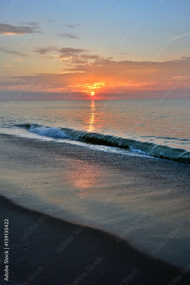 Fototapeta premium Waves Breaking Beneath a Sunrise on the Beach