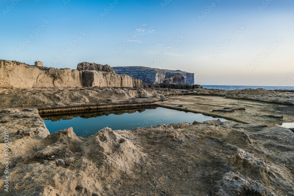 Water square pool on the eroded rocky seashore. Summer evening on Island of Malta.