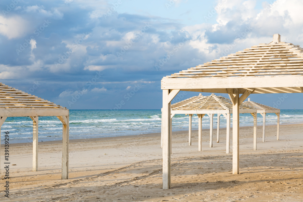 White sunshades on beautiful beach and cloudy sky. Travel and vacation concept. White sunshades on beautiful beach and cloudy sky. Travel and vacation concept.