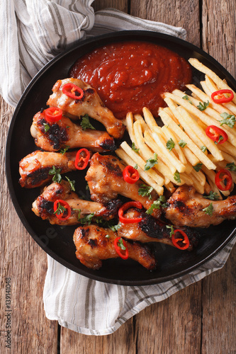 Spicy BBQ chicken wings with french fries and sauce close-up. Vertical top view