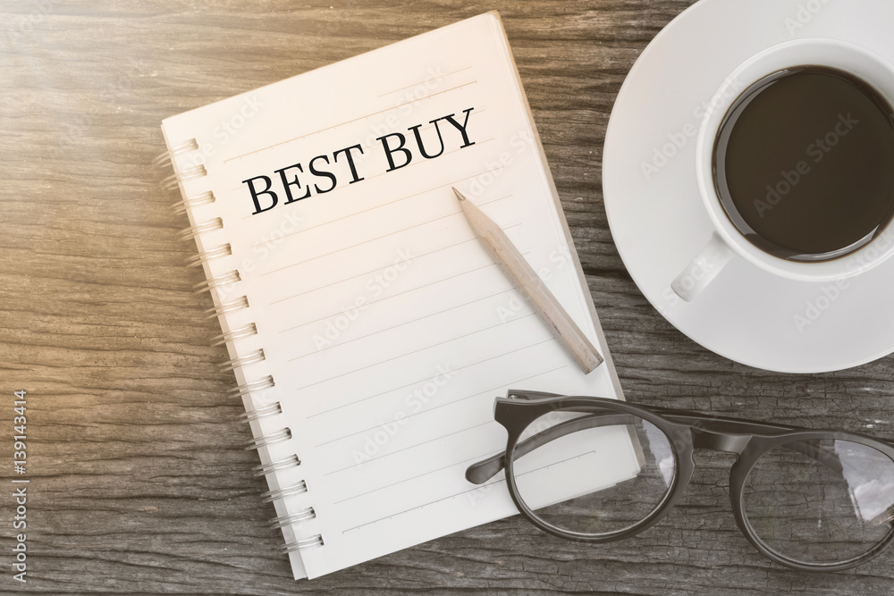 Concept BEST BUY message on notebook with glasses, pencil and coffee cup on wooden table. Concept BEST BUY message on notebook with glasses, pencil and coffee cup on wooden table.