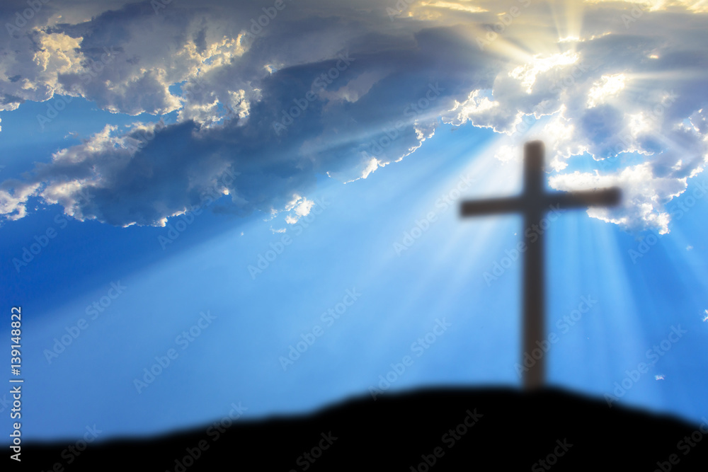 Cross on the Calvary hill with cloudy sky and sun light beams or rays. Abstract blury religious background.