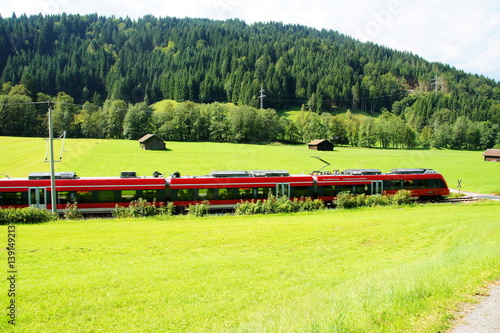 grüne Landschaft mit rotem Regionalzug bei Mittenwald in Bayern 