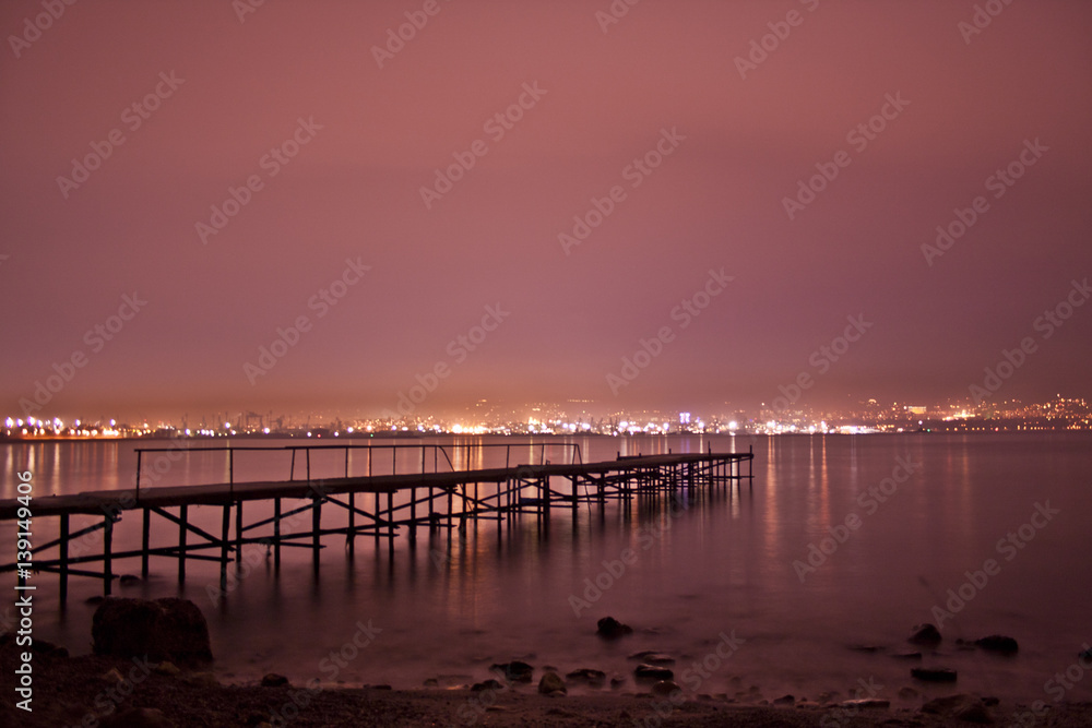 City night lights with red sky, sea and pier
