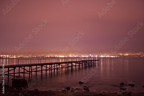City night lights with red sky, sea and pier