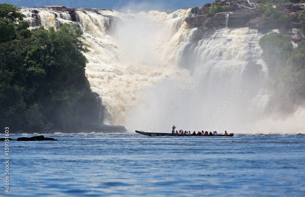 Fototapeta premium Waterfall and the boat with the tourists in the lagoon of Canaima national park - Venezuela