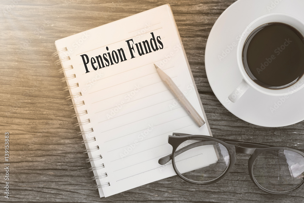Concept Pension Funds message on notebook with glasses, pencil and coffee cup on wooden table. Concept Pension Funds message on notebook with glasses, pencil and coffee cup on wooden table.