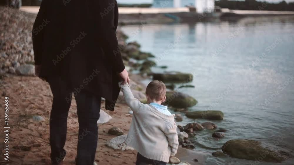 Back view of father and son on the beach holding hands and walking along the shore at sunset. Back view of father and son on the beach holding hands and walking along the shore at sunset.