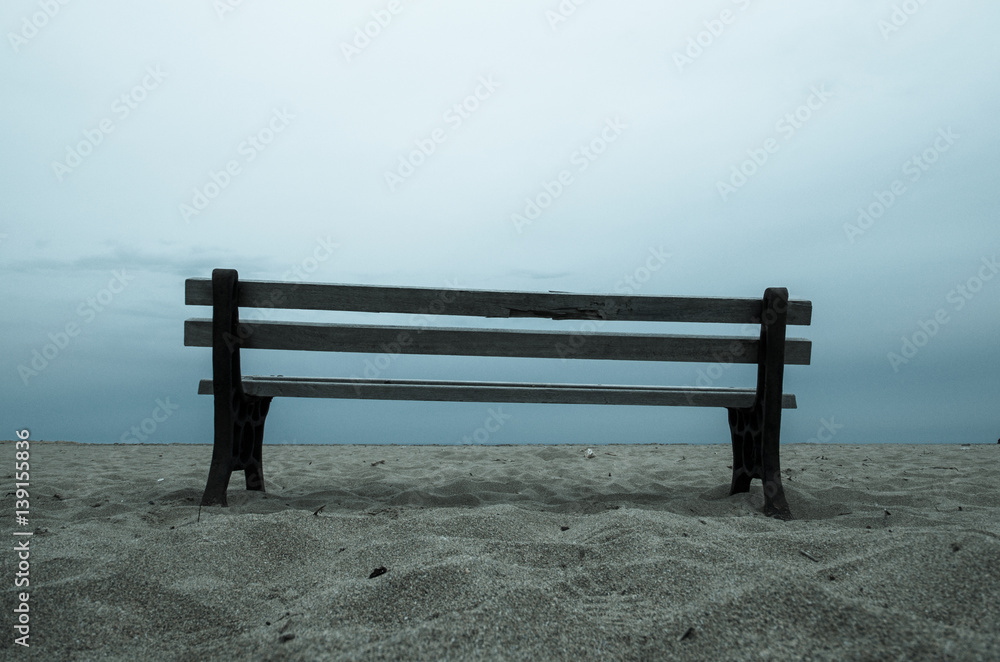 Old empty bench stands on sandy beach at a dull evening, Malia, Crete, Greece