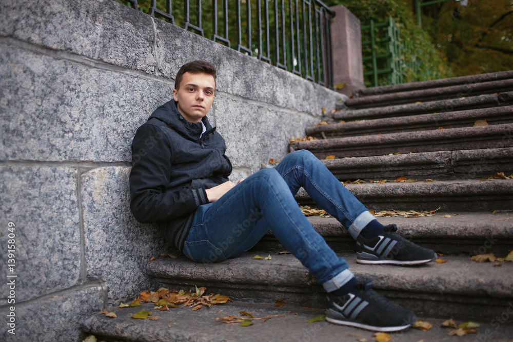 A young guy sitting on the stairs in the Park among the yellow leaves