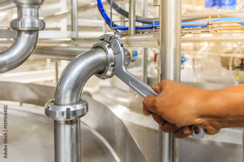 Close up shot of a hand of technician using adjustable Hook Wrench during repairing pipes at mixing tank on production line in pharmacy industry manufacture factory Close up shot of a hand of technician using adjustable Hook Wrench during repairing pipes at mixing tank on production line in pharmacy industry manufacture factory
