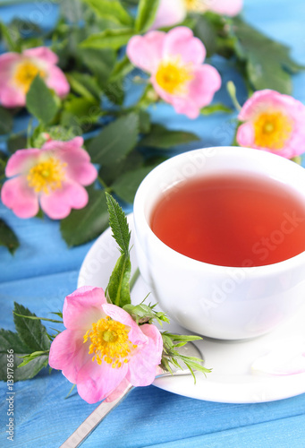 Cup of tea and wild rose flower on blue boards