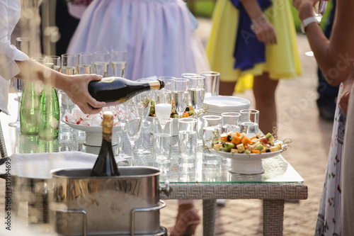 Fototapeta Naklejka Na Ścianę i Meble -  Party outdoors. People stand near the table with glasses of champagne and fruits.