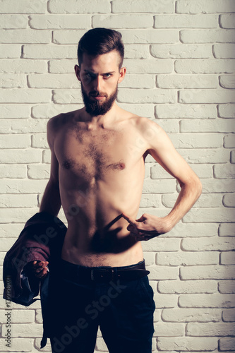 slim bearded man with thin bare torso on brick background