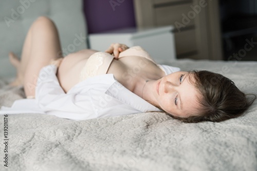 Pregnant woman in lingerie and white shirt in bed