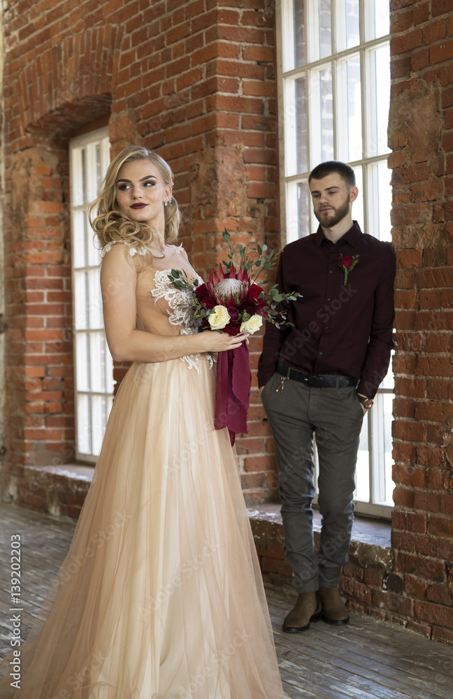 bride and groom pose near window and vintage brick wall