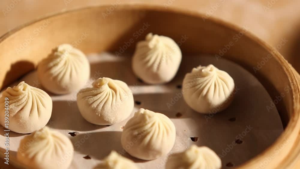 A cook is making dumplings with his hands and is placing them in a bowl. He uses a bamboo steamer basket to place it on a pot of boiling water A cook is making dumplings with his hands and is placing them in a bowl. He uses a bamboo steamer basket to place it on a pot of boiling water