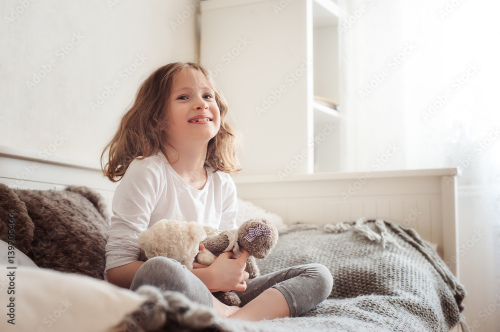 happy kid girl playing with teddy bears in her room, sitting on bed in the morning happy kid girl playing with teddy bears in her room, sitting on bed in the morning