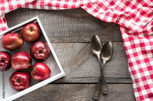 Ripe red apples in birch-box on wooden board with red checkered napkin around, and spoons and copy space for your recipe.