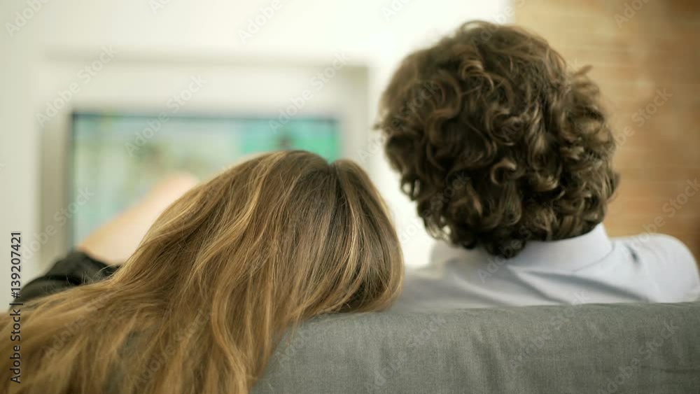 Woman lying in her boyfriend's arm and watching television together
