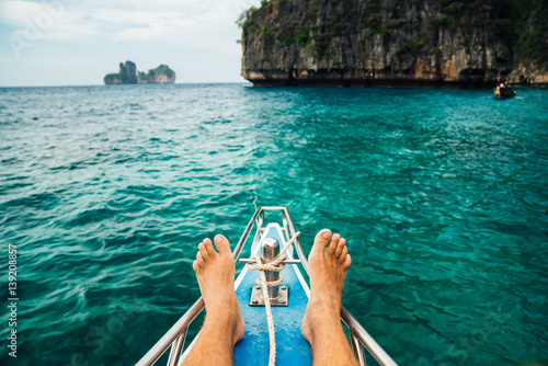 Feet resting on the tourist deck of the yacht in the turquoise sea on island background. The concept of comfort.