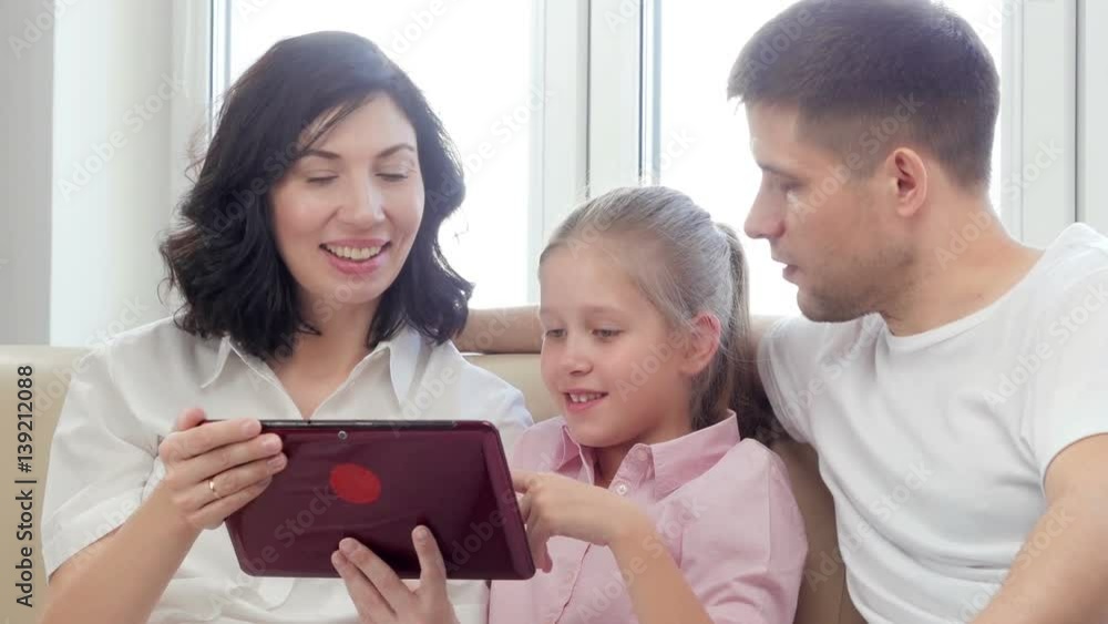Parents showing digital tablet to their daughter at home.
Parents showing digital tablet to their daughter at home.