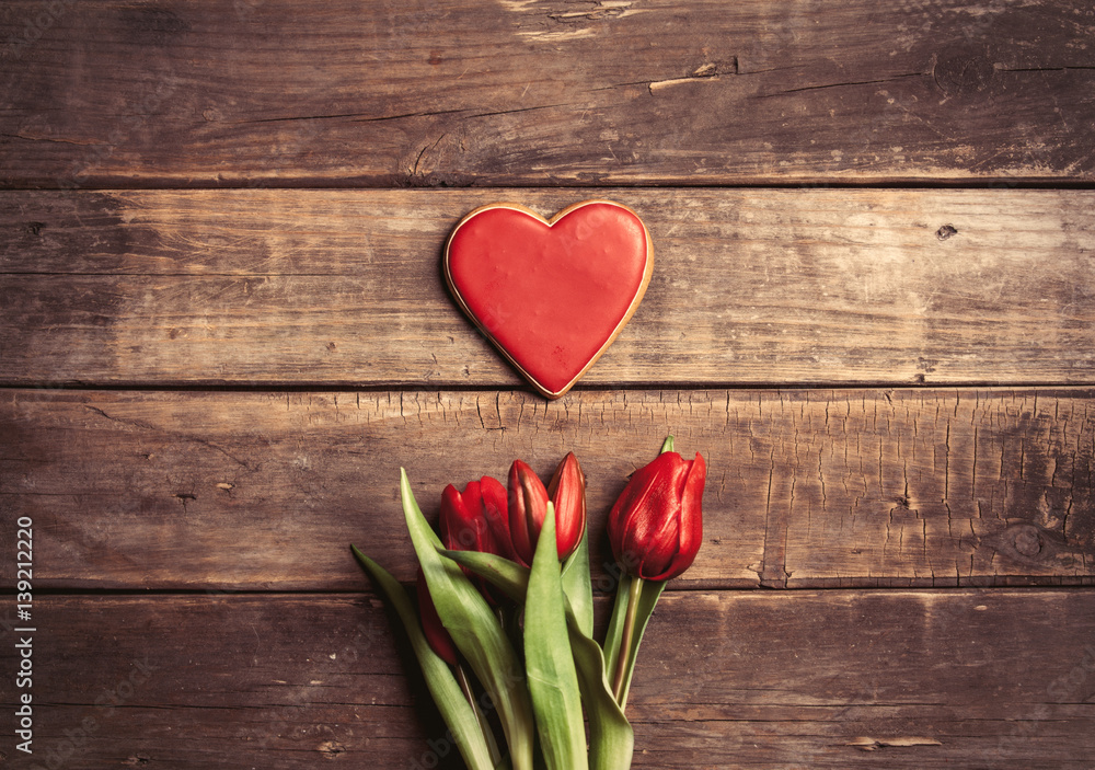 Fototapeta premium heart shaped cookie and bunch of tulips lying on the wonderful brown wooden background