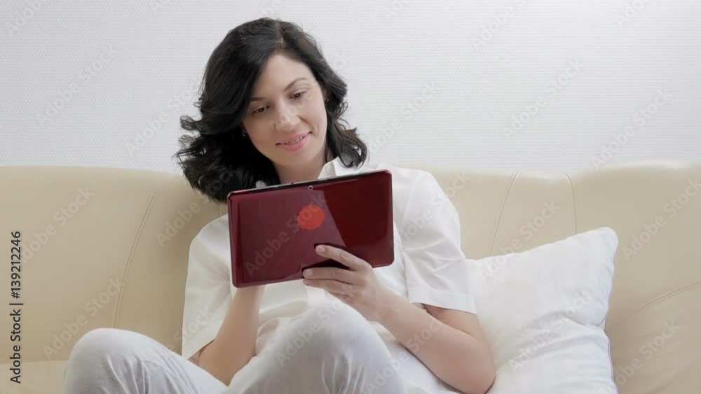 Young woman using electronic tablet sitting in sofa Young woman using electronic tablet sitting in sofa