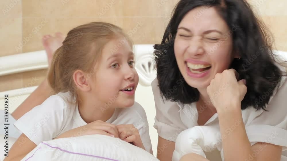 Happy little girl telling her mother a secret at home in bedroom.
Happy little girl telling her mother a secret at home in bedroom.