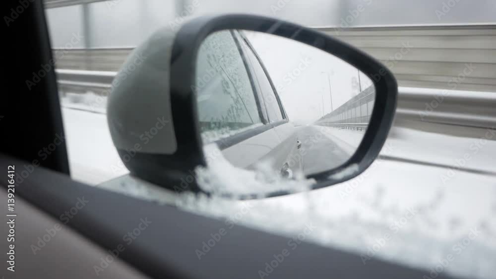 Driving on a snowy highway on a winter afternoon through a village, shot through the rearview mirror Driving on a snowy highway on a winter afternoon through a village, shot through the rearview mirror