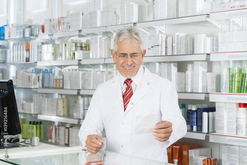 Chemist Looking At Prescription Paper At Counter Chemist Looking At Prescription Paper At Counter