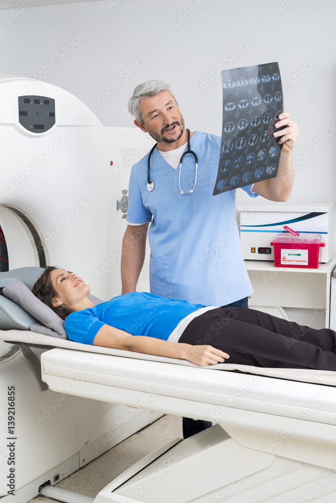Fototapeta premium Doctor Explaining X-ray To Patient Lying On MRI Machine