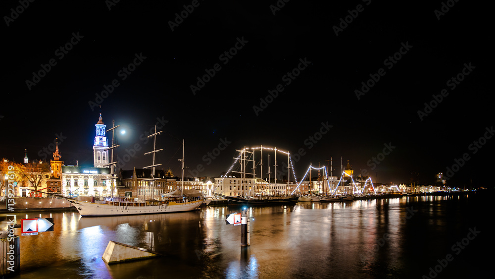 Obraz premium Overlooking the city front and the quay of the city of Kampen at the river IJssel. Long Exposure photography with just lighted boats along the quay. Overijssel - Netherlands. 
