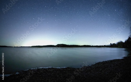 Peaceful night scene with starry sky at a lake in Finland. Reflection of stars on the still water of the lake. © Teemu Tretjakov