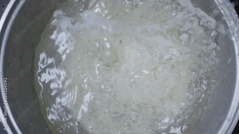 Slow mo white long-grain rice falls into a cast-iron pot with water Slow mo white long-grain rice falls into a cast-iron pot with water