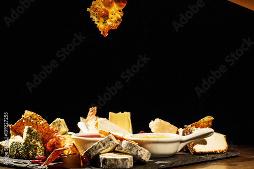 Someone holds piece of baked cheese with species over plate with different kinds of cheese