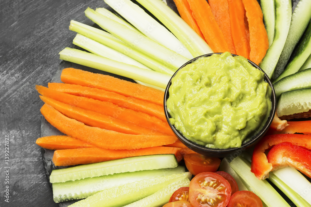 Traditional Latin American sauce guacamole in a bowl and various vegetables (carrots, tomatoes, cucumbers, celery) on a dark background. Traditional Latin American sauce guacamole in a bowl and various vegetables (carrots, tomatoes, cucumbers, celery) on a dark background.