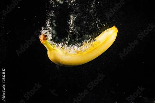 Sprkling yellow banana falls in water on black background photo