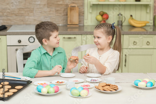 Cute kids baked cookies and tasting it at the table in the home kitchen