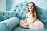 Gorgeous little girl with dark blonde hair lies on blue couch