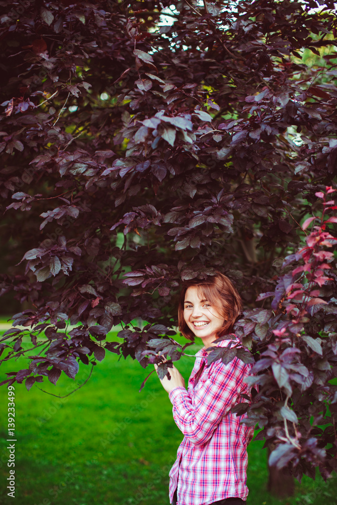 Joyful young girl with red hair stnds under dakr green leaves Joyful young girl with red hair stnds under dakr green leaves