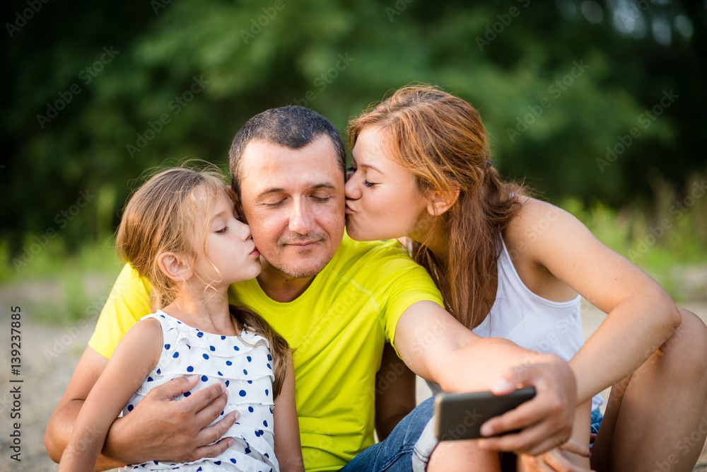 Father being kissed by daughters while taking a selfie