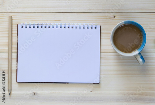 A Pencil with notebook and coffee cup on the wooden background.