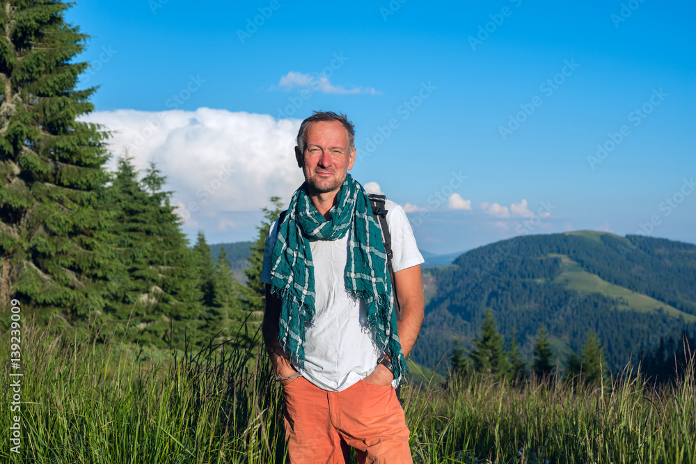 Smiling man traveler is standing on the alpine meadow Smiling man traveler is standing on the alpine meadow