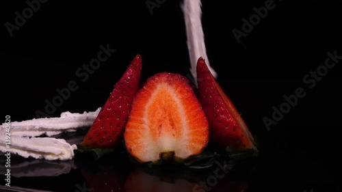 Whipped cream poured over spinning sliced rip strawberries isolated on black background. Slow motion. Healthy diet. Close-up rotation in full HD footage 1920x1080
